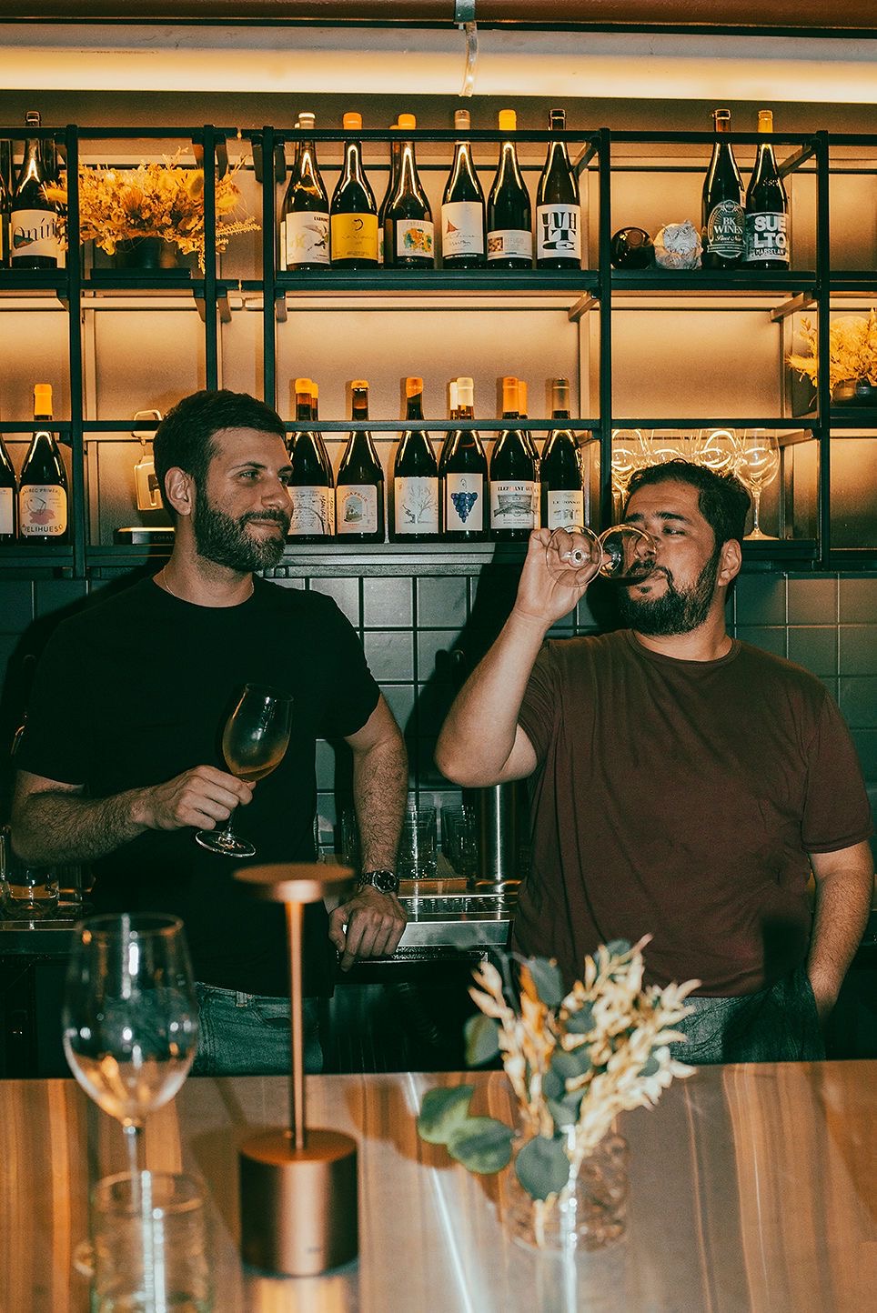 Luciano y Luis tomando una copa de vino detrás de la barra de un bar de vinos